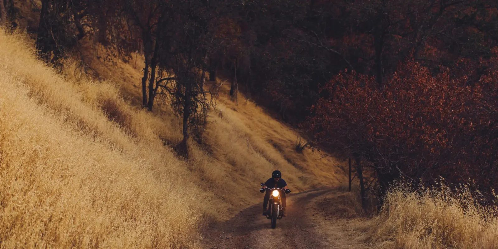 Moto avanzando por un camino de tierra entre pastizales y árboles otoñales
