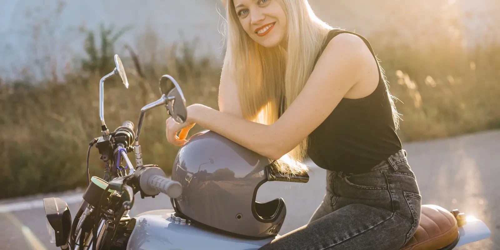 Mujer sentada en una moto con el casco apoyado en el tanque, a la luz del atardecer