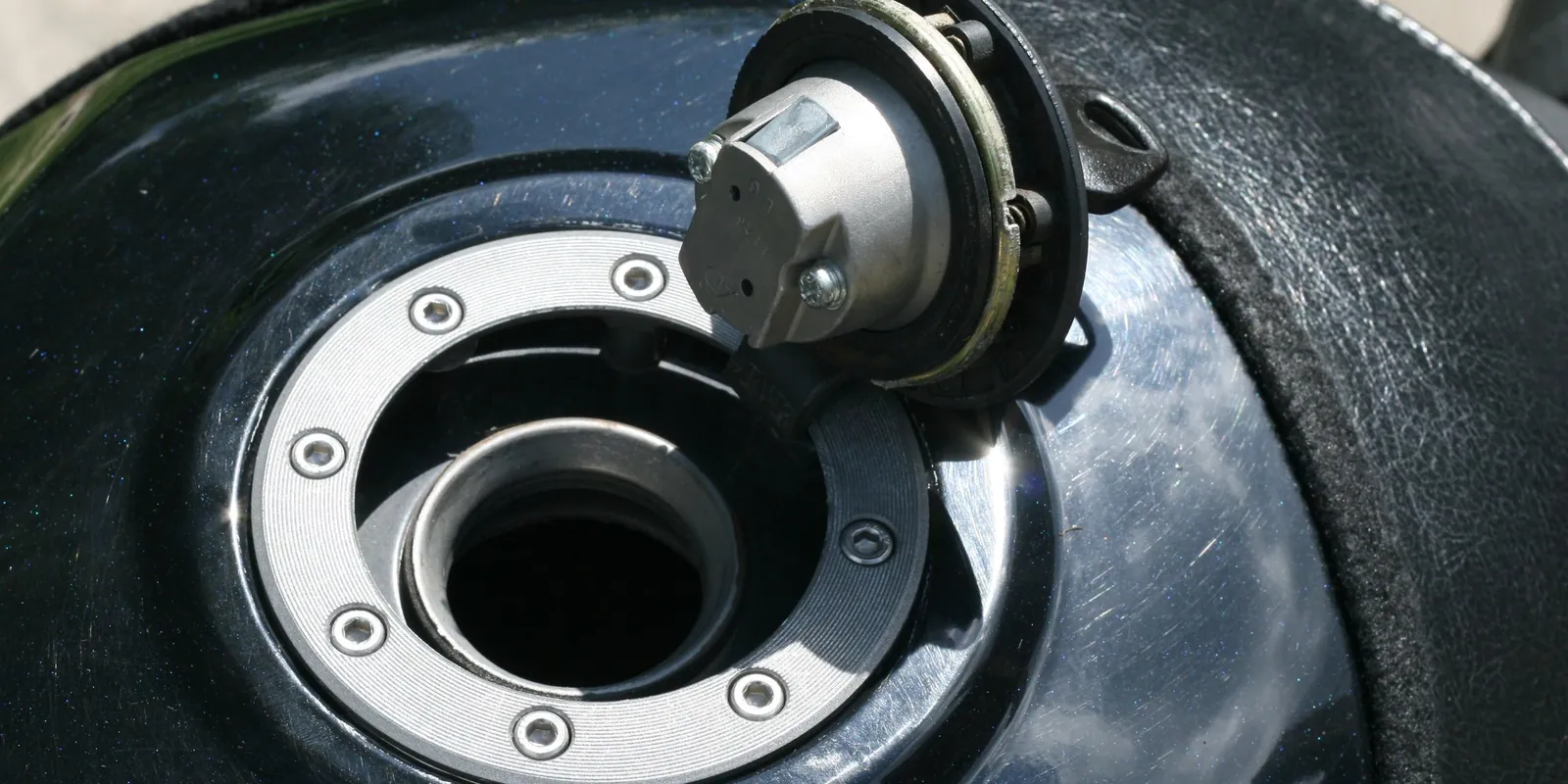 Tapa de tanque de combustible abierta sobre el tanque negro de una moto